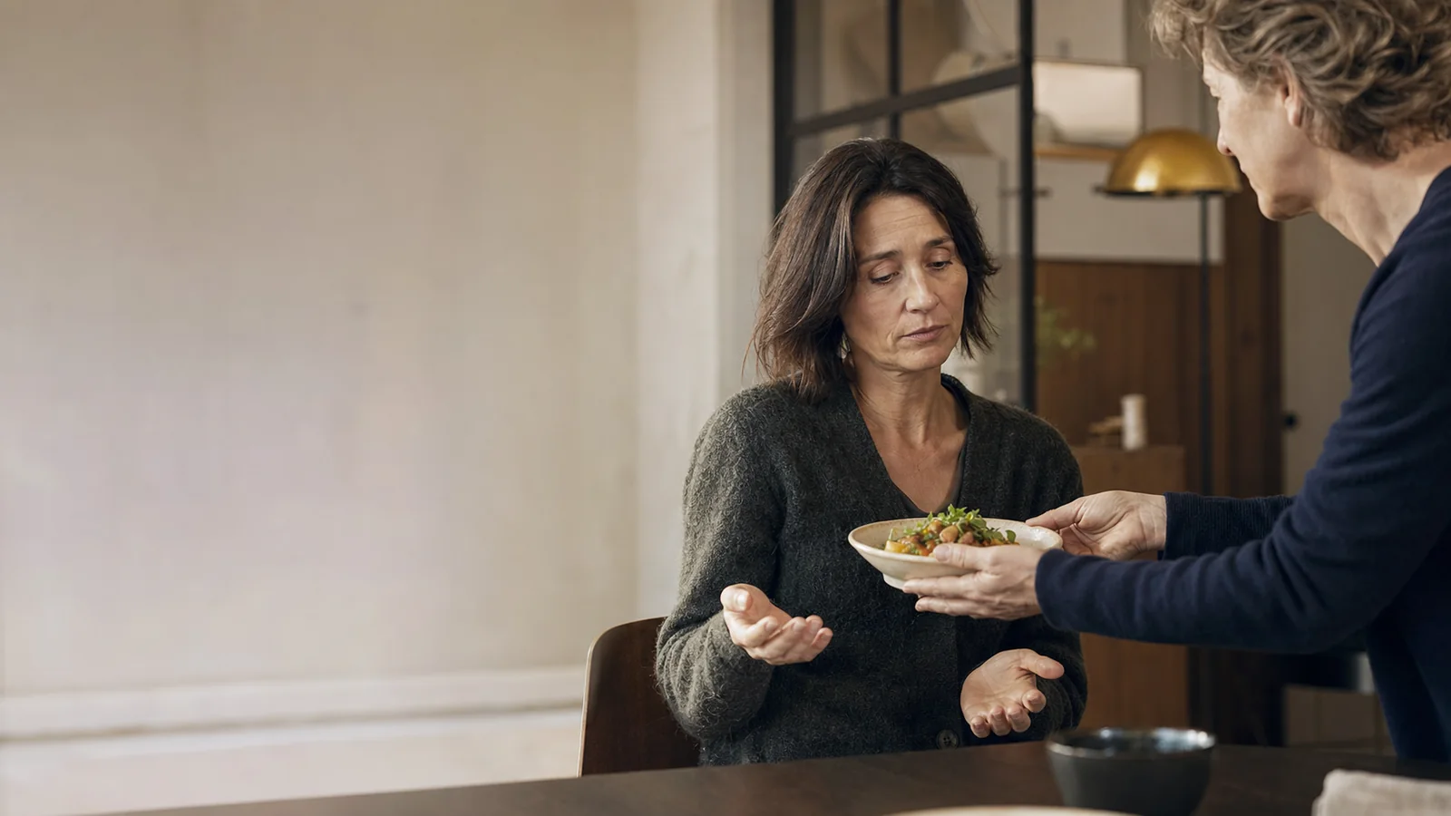 Une femme hésite à recevoir un plat que lui tend une autre personne.