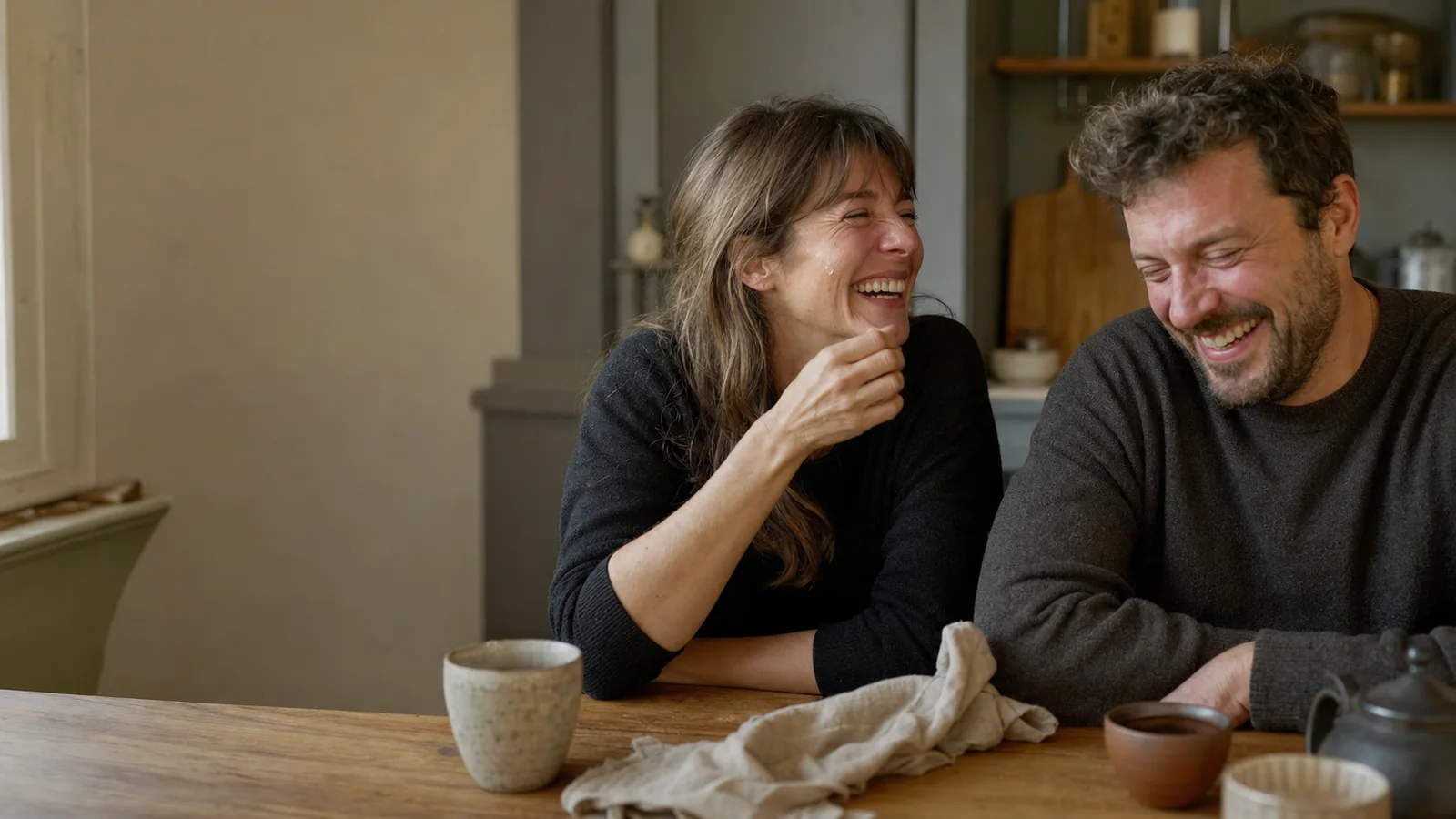 Une femme et un homme reprennent leur souffle après un éclat de rire autour d’une table.